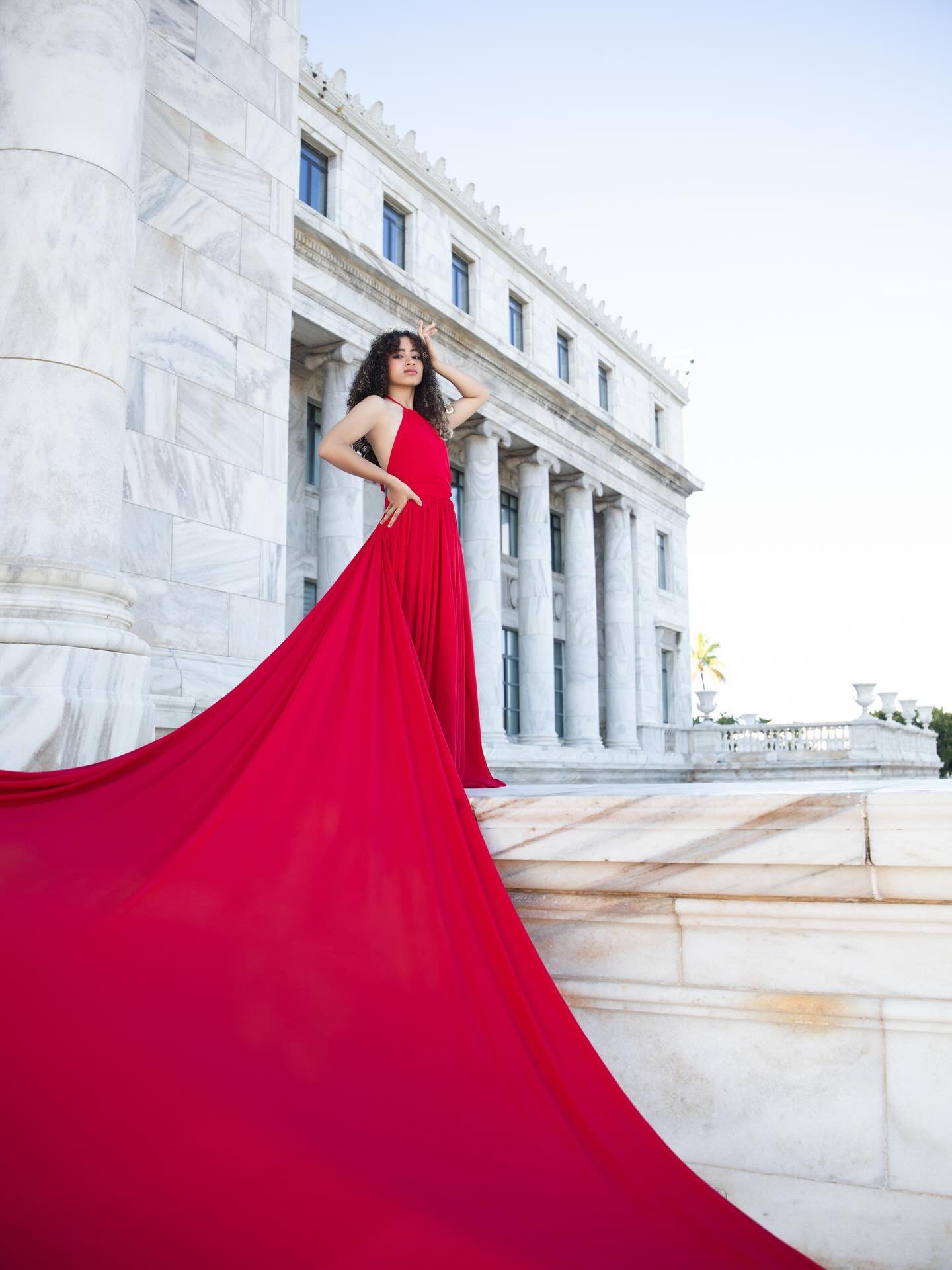 Quinceañera in a flowing red gown before marble architecture