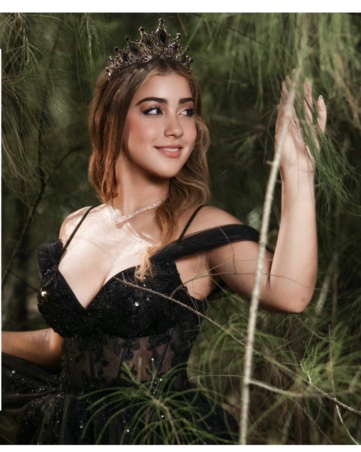 Quinceañera wearing a dark crown and black dress among pine branches